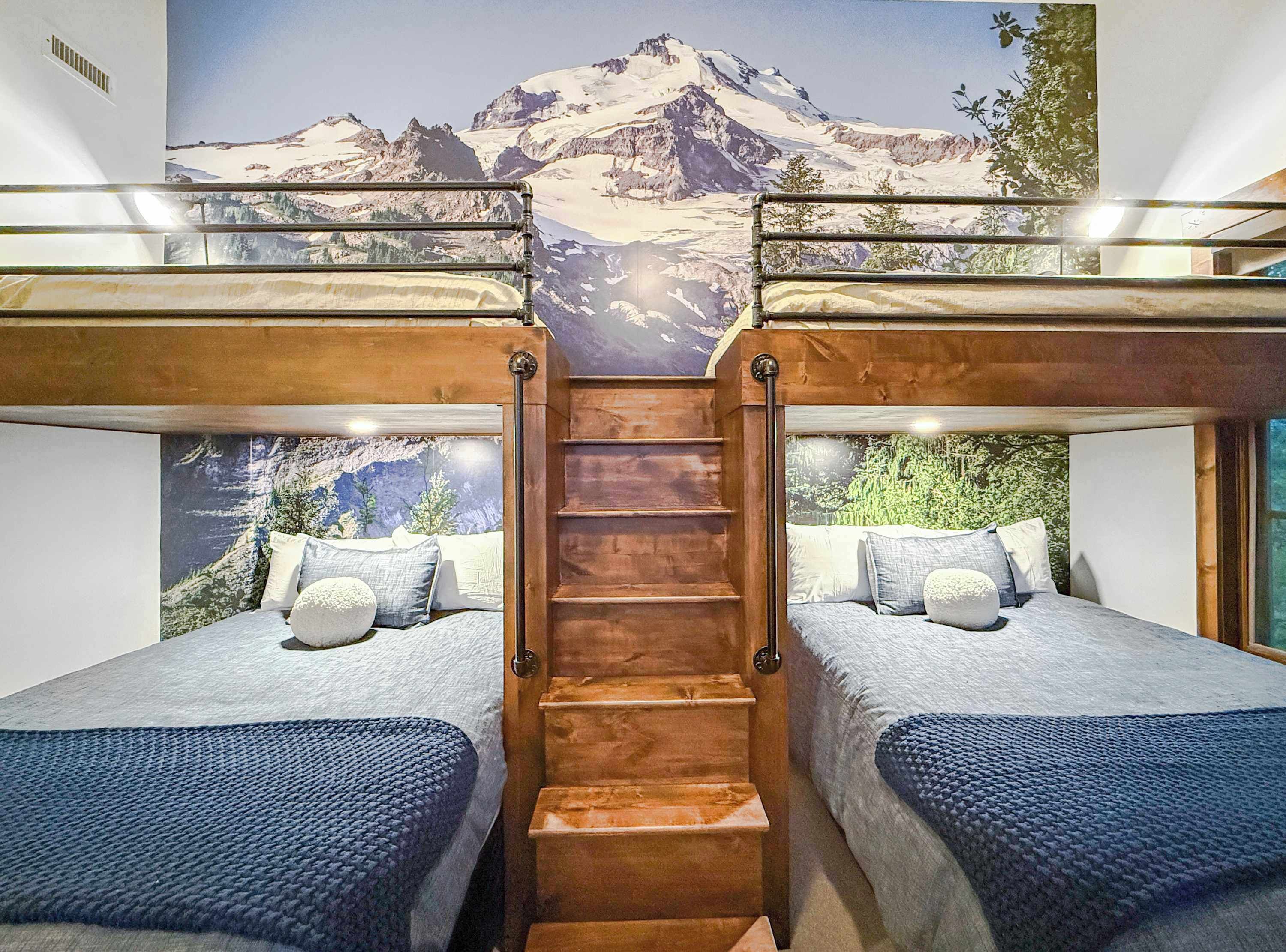 A bunk bed room with a mountain view mural, wooden staircase, and two beds with blue bedding.