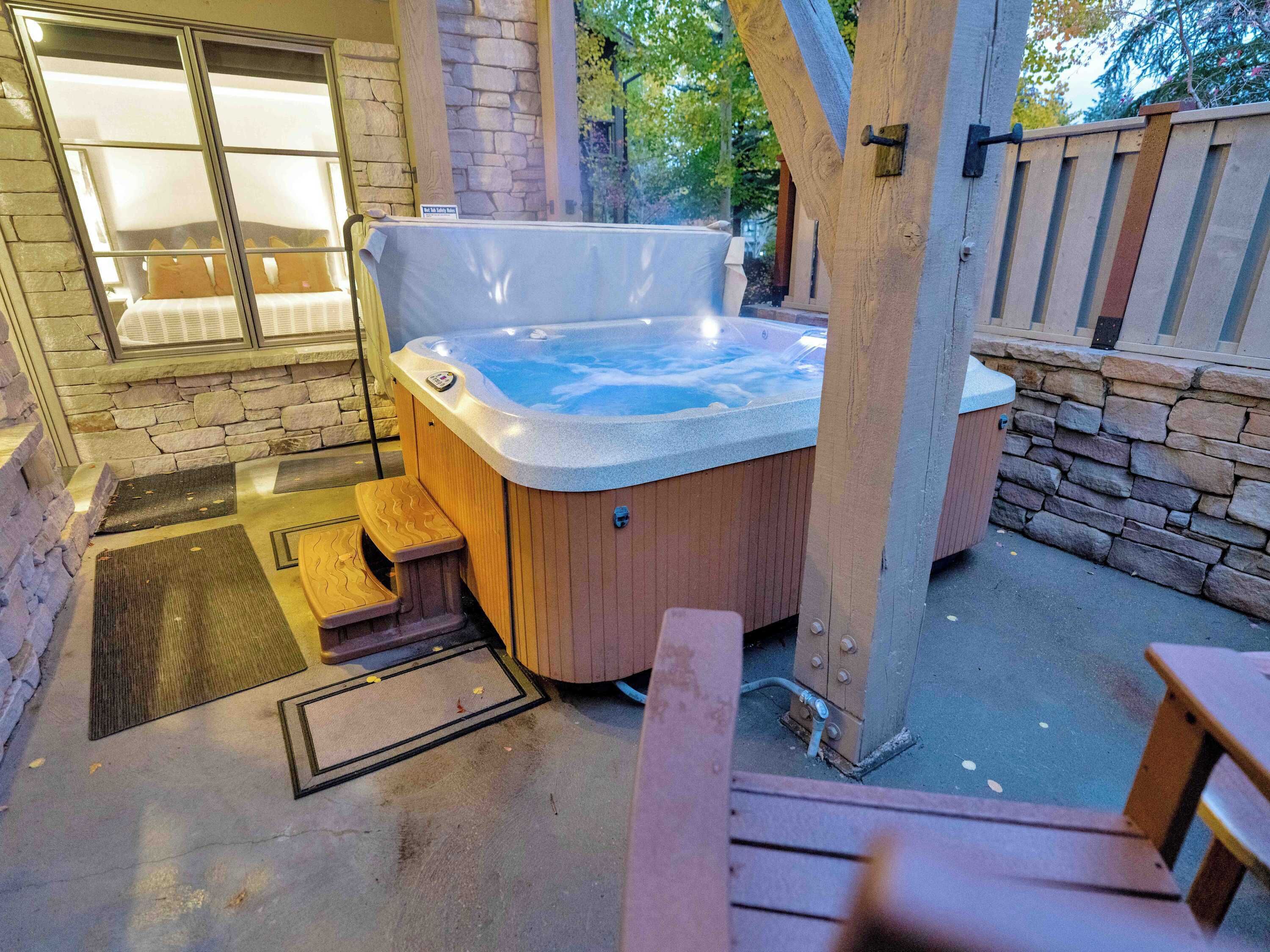 A hot tub with wooden steps and a stone wall backdrop.