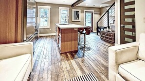 A spacious living area with a wooden floor, a central island with a sink, a staircase, and a view of the outdoors. - A romantic getaway that's steps from Main Street. (Park City)