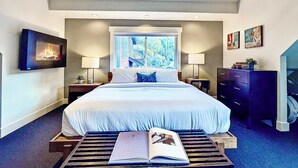 A bedroom with a large bed, two bedside tables, a dresser, a window with a view, and a painting on the wall. - A romantic getaway that's steps from Main Street. (Park City)