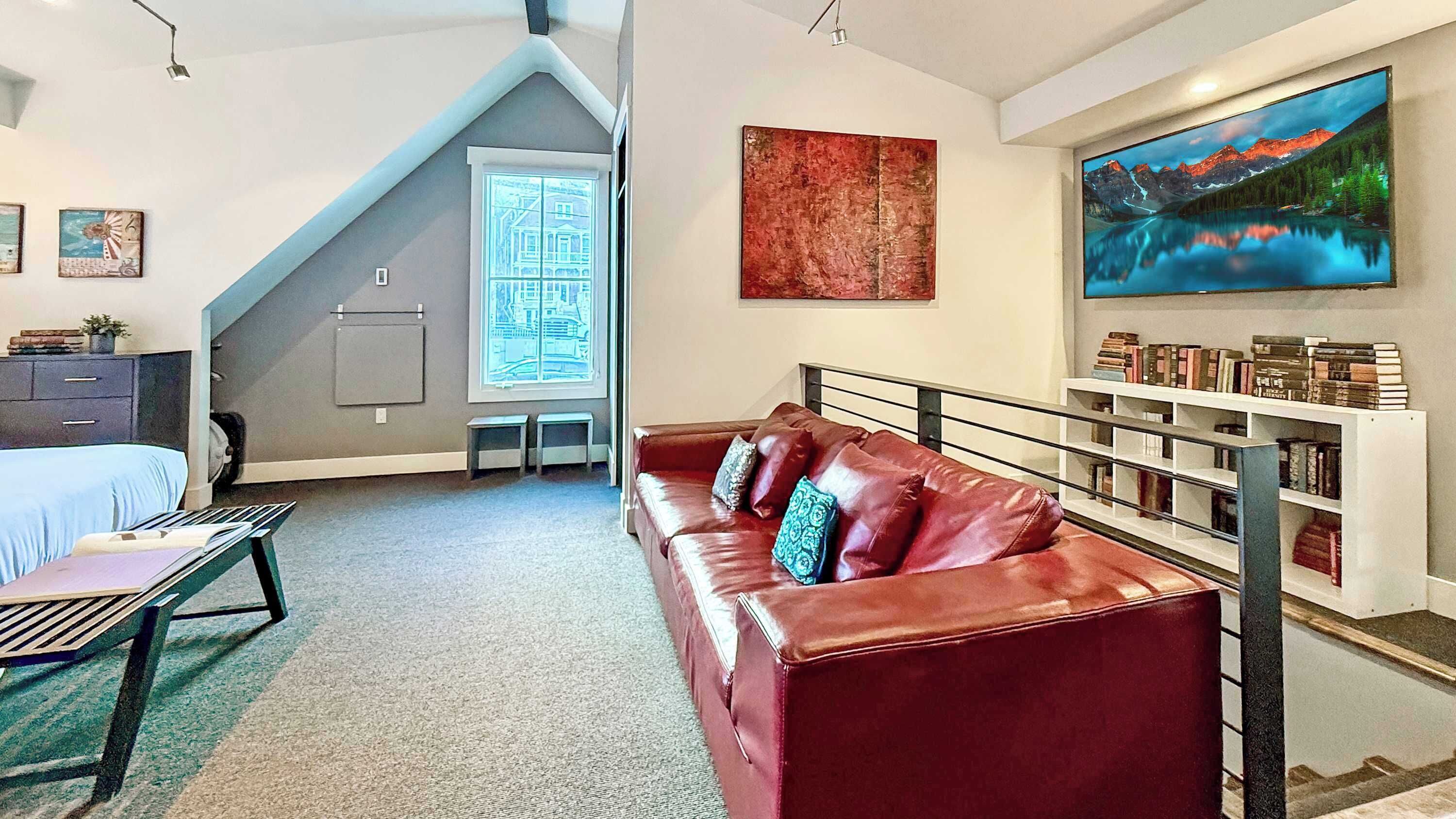 Una habitación moderna con un sofá de cuero rojo, un escritorio, una estantería y un ventanal con vistas a montañas.