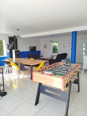 A modern living room with a foosball table, a dining area with chairs, a sofa, and a TV.