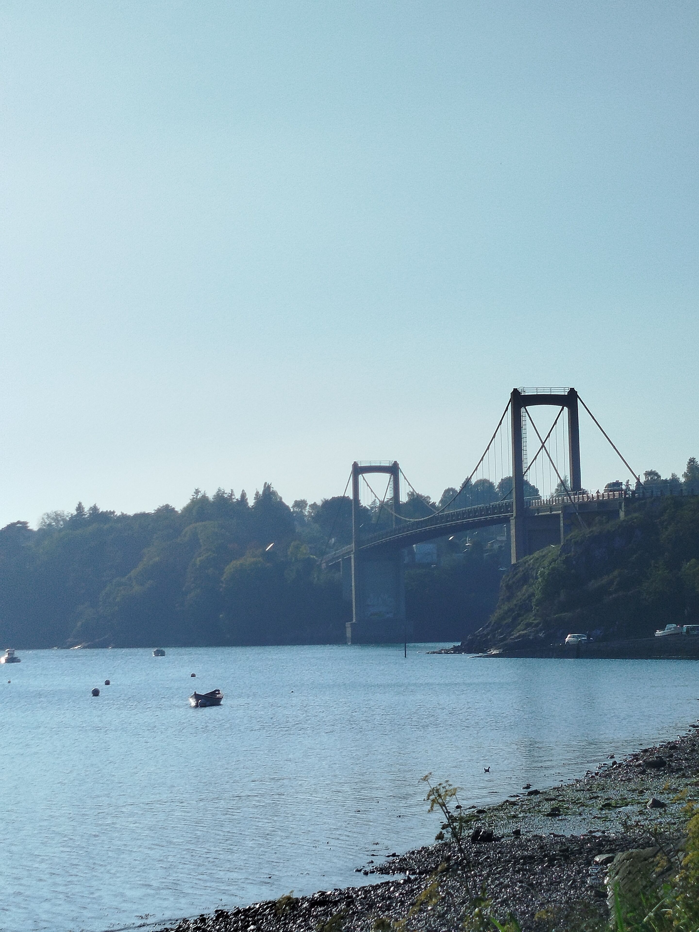 Eine große Hängebrücke über einem Wasserlauf mit Booten und einer felsigen Küstenlinie.