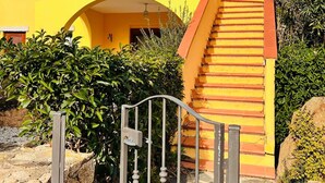 Ein zweistöckiges Gebäude mit einer gelben Fassade, einem hölzernen Balkon und einer Steintreppe, die zu der oberen Etage führt.