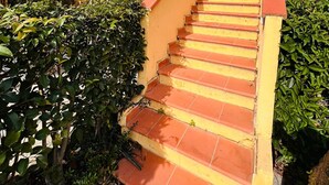 Eine Treppe führt zu einem Balkon mit einem Metallgeländer, umgeben von Grünpflanzen.