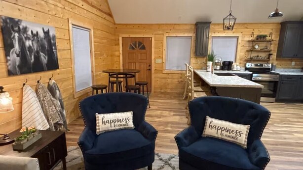 A cozy cabin interior with two dark blue armchairs, a wooden dining table, and a kitchen area. - Relax & Recharge at Firefly Cabin (Russellville)