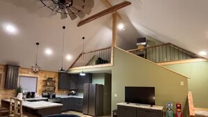 A spacious living area with a high ceiling, wooden flooring, a dining area with a table and chairs, a kitchen with modern appliances, and a staircase leading to an upper level. - Relax & Recharge at Firefly Cabin (Russellville)