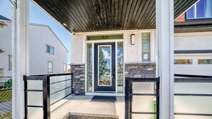 Uma casa moderna com varanda frontal, porta preta e parede de pedra decorativa.