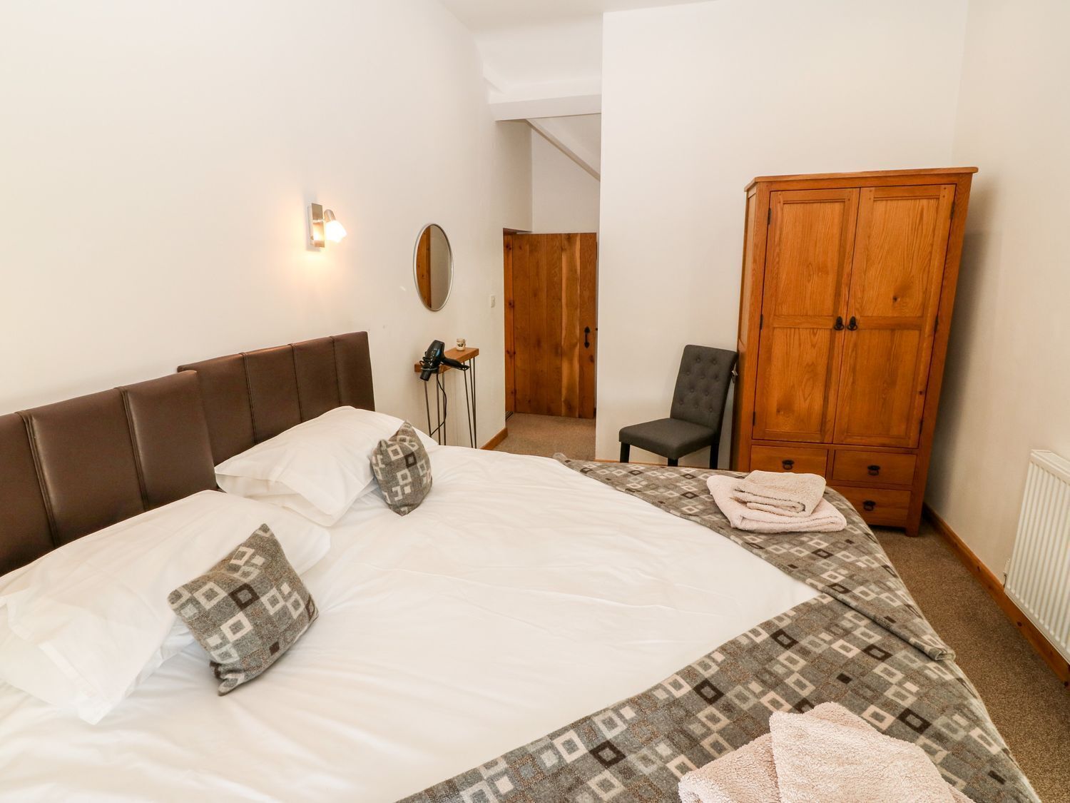 A bedroom with a large bed, a wardrobe, a chair, and a mirror.