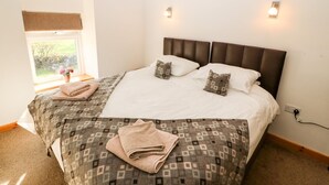 Un lit bien fait, avec une couvre-lit à motifs, deux oreillers et une serviette pliée posée sur le sol.