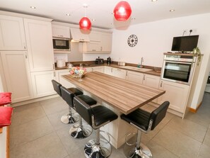 Uma cozinha moderna com uma ilha central, banquetas, micro-ondas, forno e um relógio na parede.