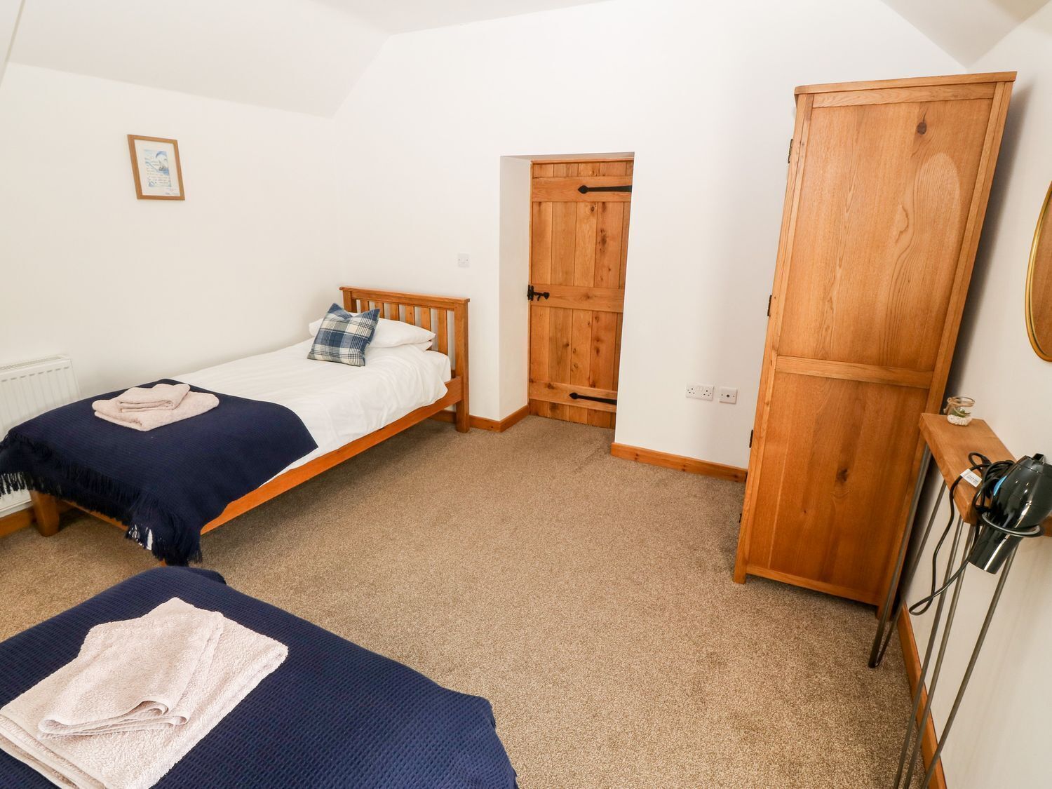 A bedroom with two single beds, a wooden wardrobe, a door, and a small table with a lamp.