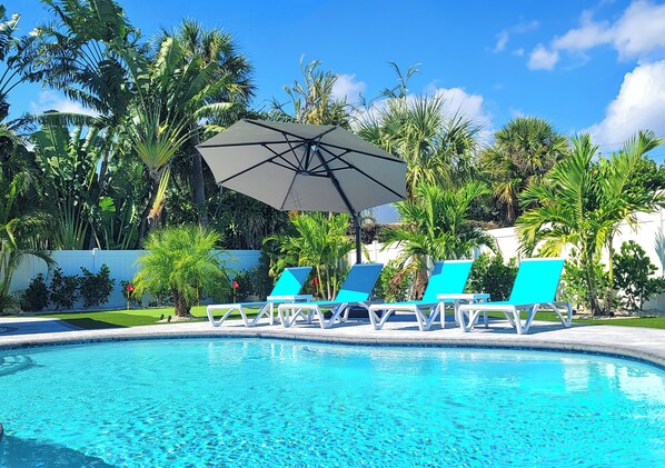 A swimming pool with lounge chairs and an umbrella.