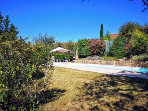 Un jardin avec une piscine, un mur en pierre et un espace patio aménagé avec des chaises et une table.