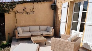 Eine Terrasse mit einer Sitzecke, zwei Korbstühlen und einem kleinen Tisch.