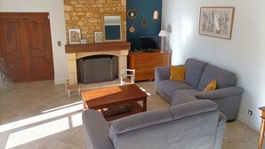 Ein Wohnzimmer mit Kamin aus Stein, einem grauen Sofa, einem Holztisch und einem Fernseher auf einer Holzkommode.