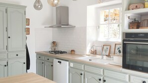 Une cuisine avec des meubles blancs, une table en bois, une cuisinière, un lave-vaisselle et des luminaires suspendus.