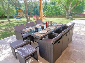 Un espace de restauration en plein air avec une table à plateau de verre, entourée de chaises en osier et d’un banc assorti.