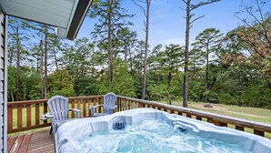 A hot tub on a wooden deck with two Adirondack chairs, surrounded by tall trees and a clear sky. - Lake Retreat w/ Hot Tub, Game Room & Grill (Rogers)