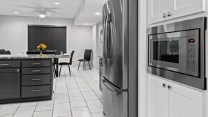 A modern kitchen with a stainless steel refrigerator, a built-in microwave, and a dining area with a table and chairs. - Lake Retreat w/ Hot Tub, Game Room & Grill (Rogers)