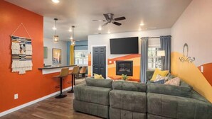 A modern living room with a green sofa, orange walls, and a ceiling fan. - Game room+Hot tub+Mtn views+Parking+Kid-friendly (Moab)