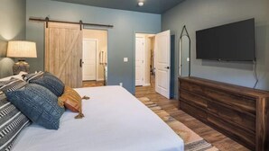 A bedroom with a bed, a dresser, a TV, and a sliding barn door. - Game room+Hot tub+Mtn views+Parking+Kid-friendly (Moab)