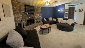 Un salon doté d’une cheminée en briques, d’un téléviseur à écran plat fixé au-dessus, de deux canapés sombres, d’une table basse ronde et d’un mur d’accent bleu.