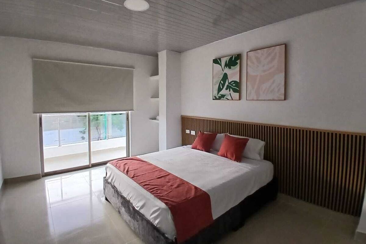 Un dormitorio moderno con una cama grande, un ventanal corredero a un balcón y dos cuadros en la pared.