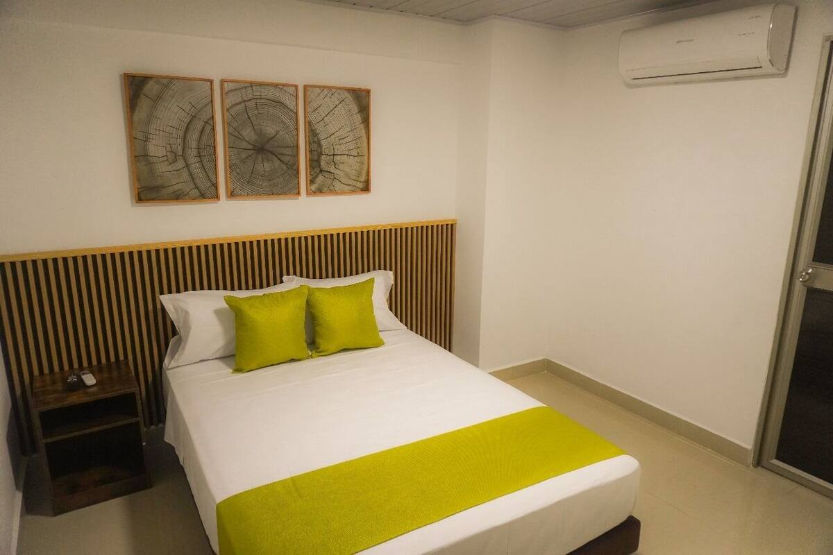 Una habitación de hotel con cama, mesita de noche y aire acondicionado instalado en la pared.