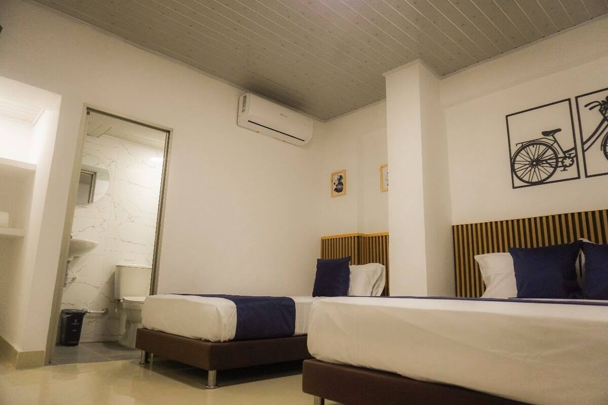 Habitación de hotel con dos camas, cabecero de madera, un espejo y aire acondicionado instalado en la pared.