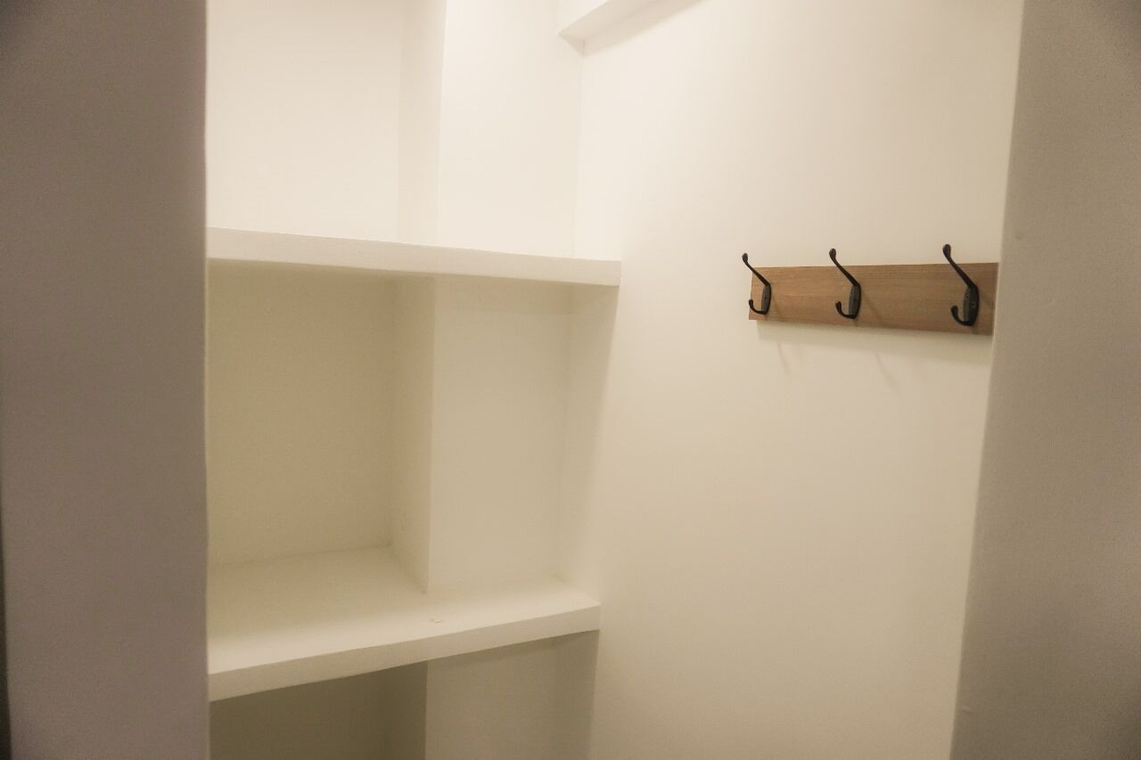A room with white walls and a wooden shelf with hooks.