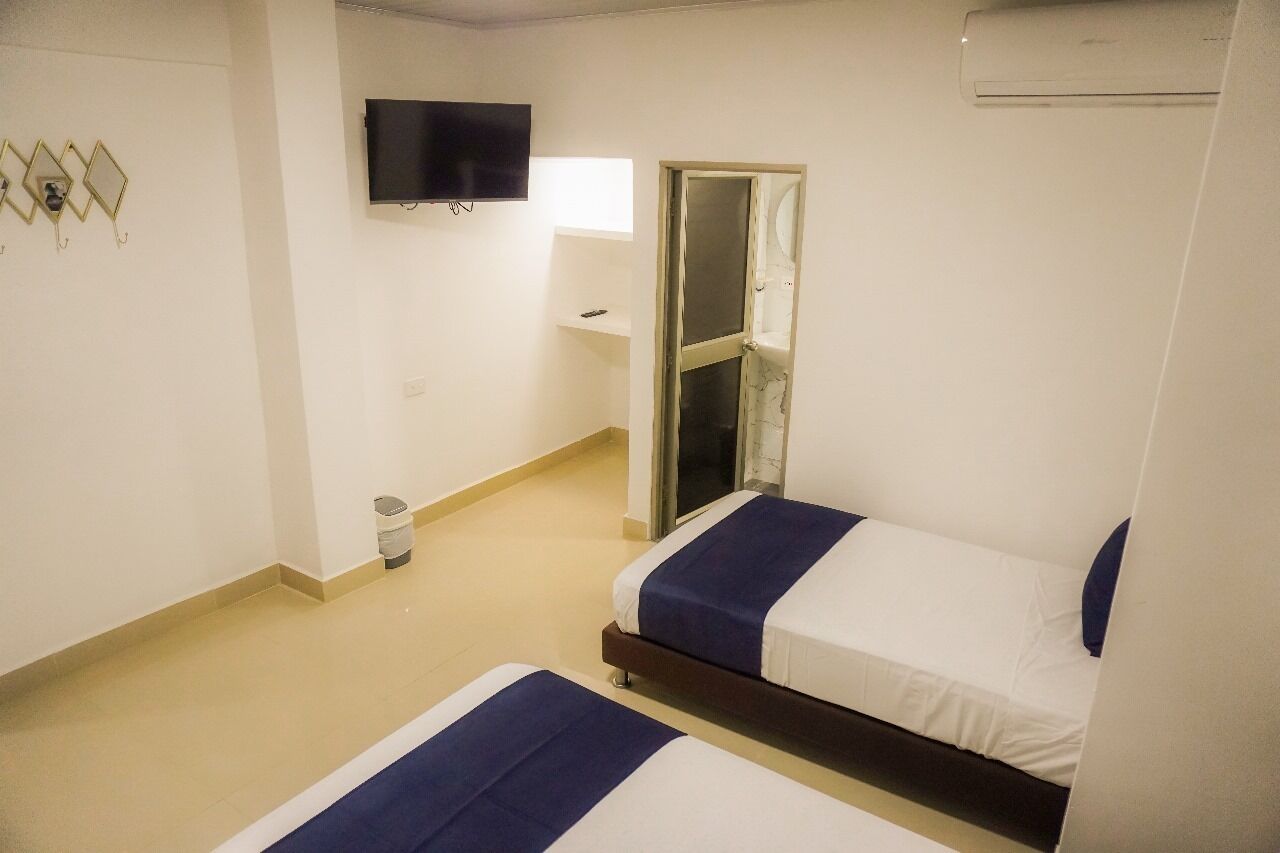 A hotel room with two beds, a TV, a small trash bin, and a window with a view.