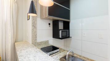 Cucina con piano di lavoro in granito, forno a microonde integrato, lampada a sospensione nera e lavello in acciaio inossidabile.