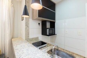 A kitchen with a granite countertop, a built-in microwave, a black hanging light fixture, and a stainless steel sink. - Apt in Downtown 150m From the Sea Tib0404 (Guarapari)
