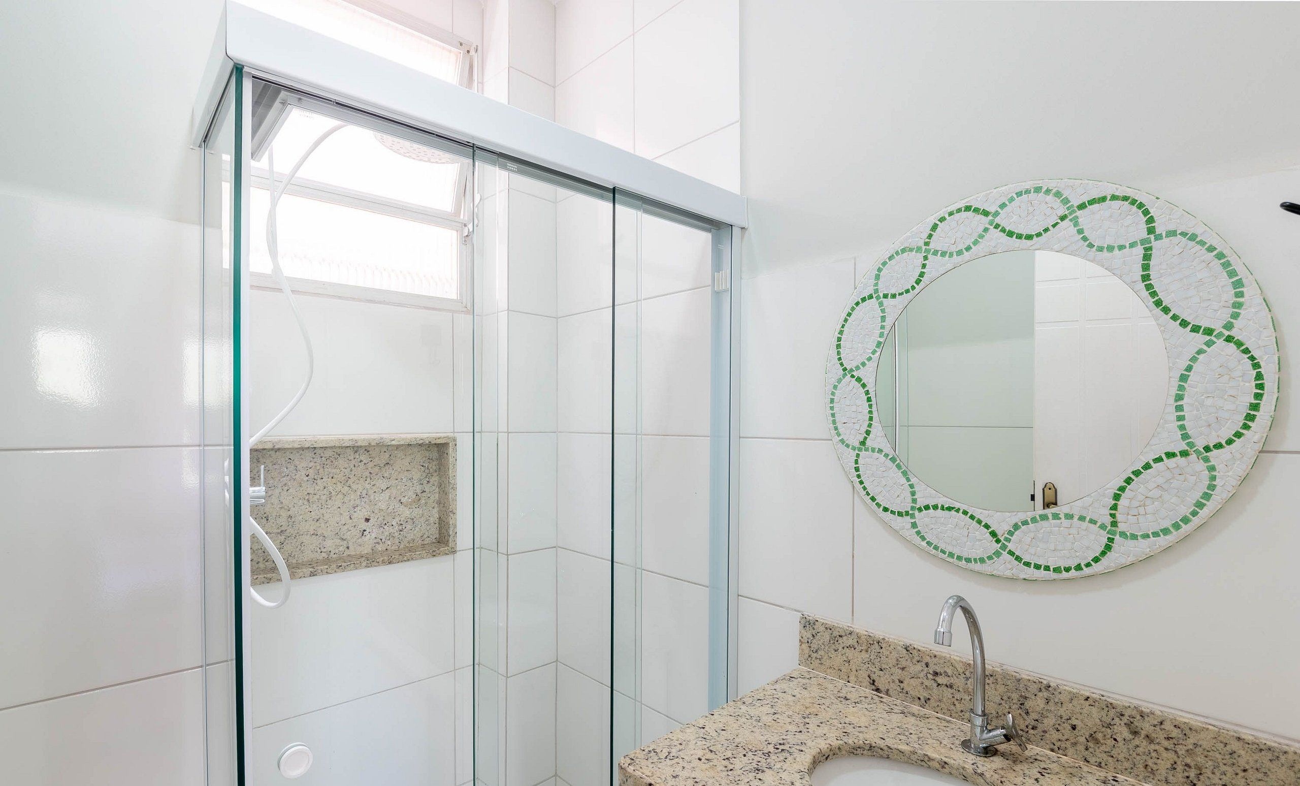 Un bagno moderno con box doccia in vetro, un piano di lavoro in granito e uno specchio decorato con mosaici.