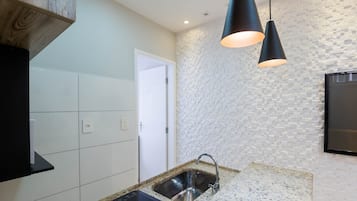 A modern kitchen with white tiles, a granite countertop, a black induction cooktop, a stainless steel sink, and a textured wall.