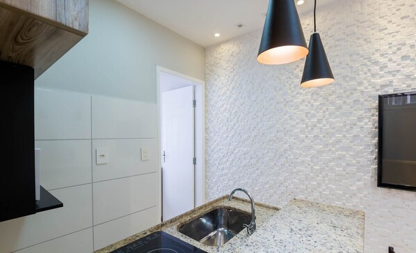 A modern kitchen with white tiles, a granite countertop, a black induction cooktop, a stainless steel sink, and a textured wall.