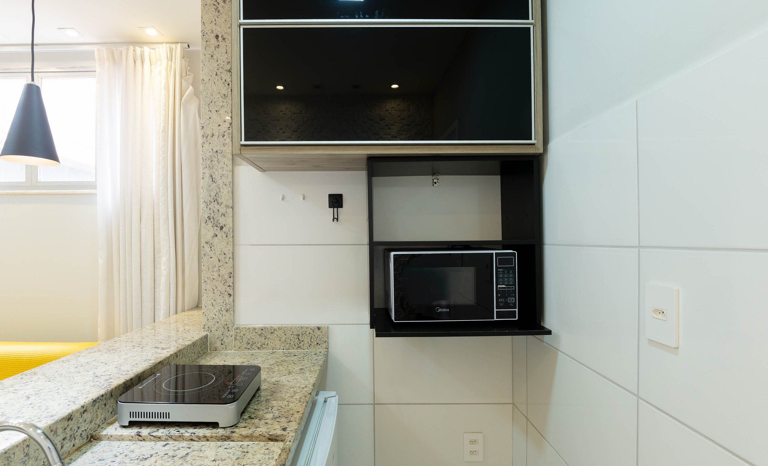 A compact kitchen with a built-in microwave, a countertop induction cooktop, and a small sink.