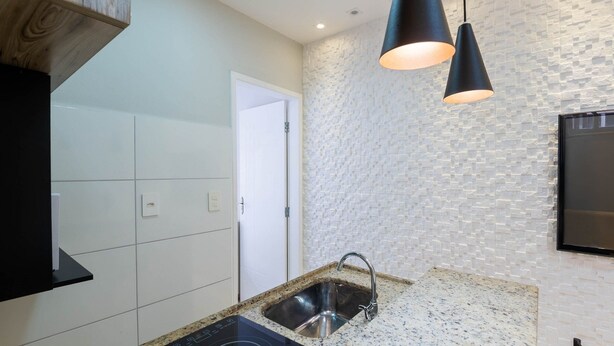 A modern kitchen with white tiles, a granite countertop, a black induction cooktop, a stainless steel sink, and a textured wall. - Apt in Downtown 150m From the Sea Tib0404 (Guarapari)