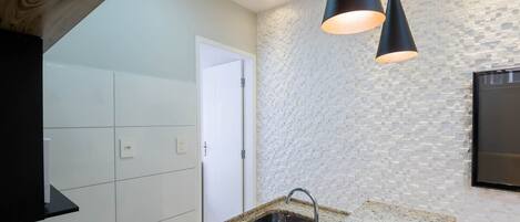 Una cocina moderna con baldosas blancas, encimera de granito, placa de inducción negra, pileta de acero inoxidable y pared con textura.