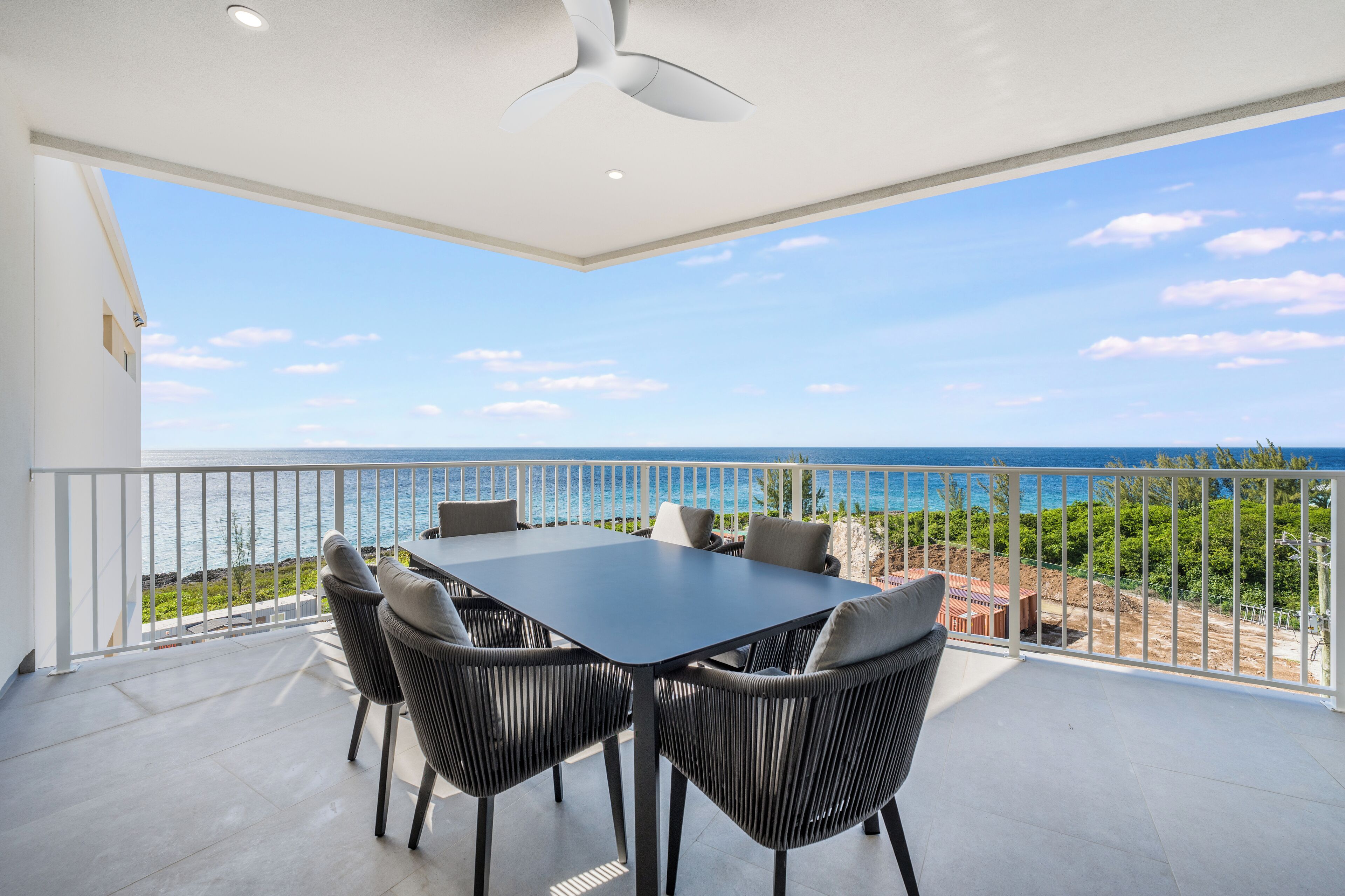 Een balkon met een tafel en stoelen, een plafondventilator en uitzicht op zee.