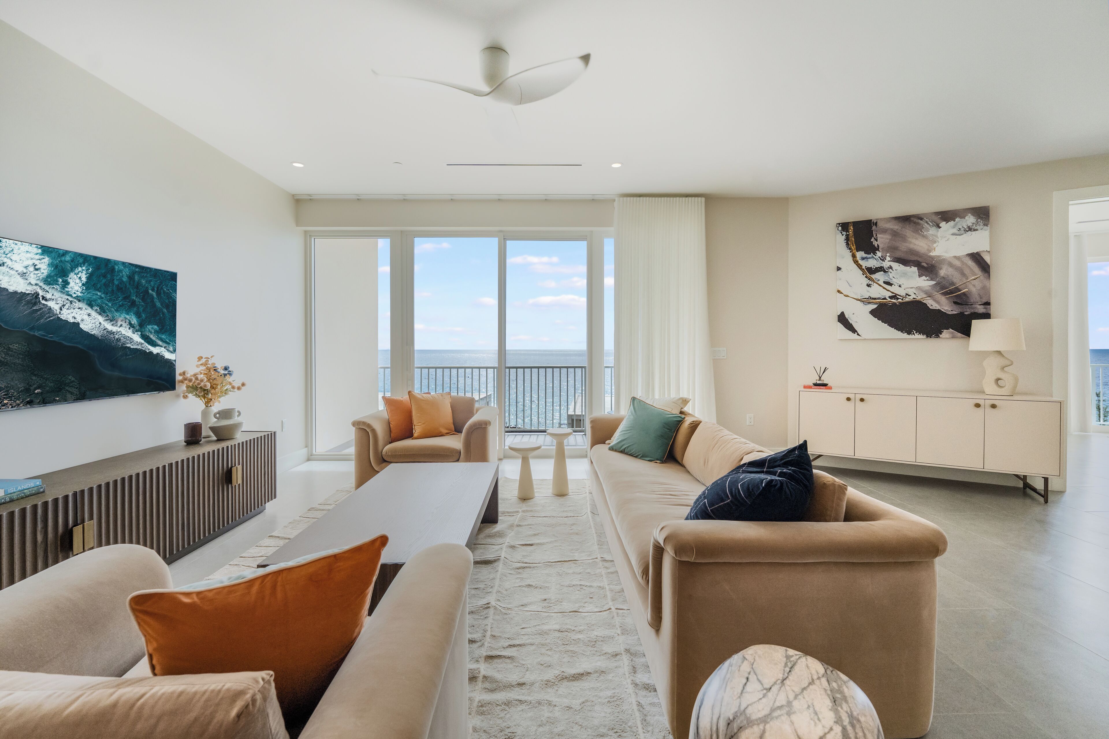 Una sala de estar moderna con un ventanal grande, un ventilador de techo y vista al mar.
