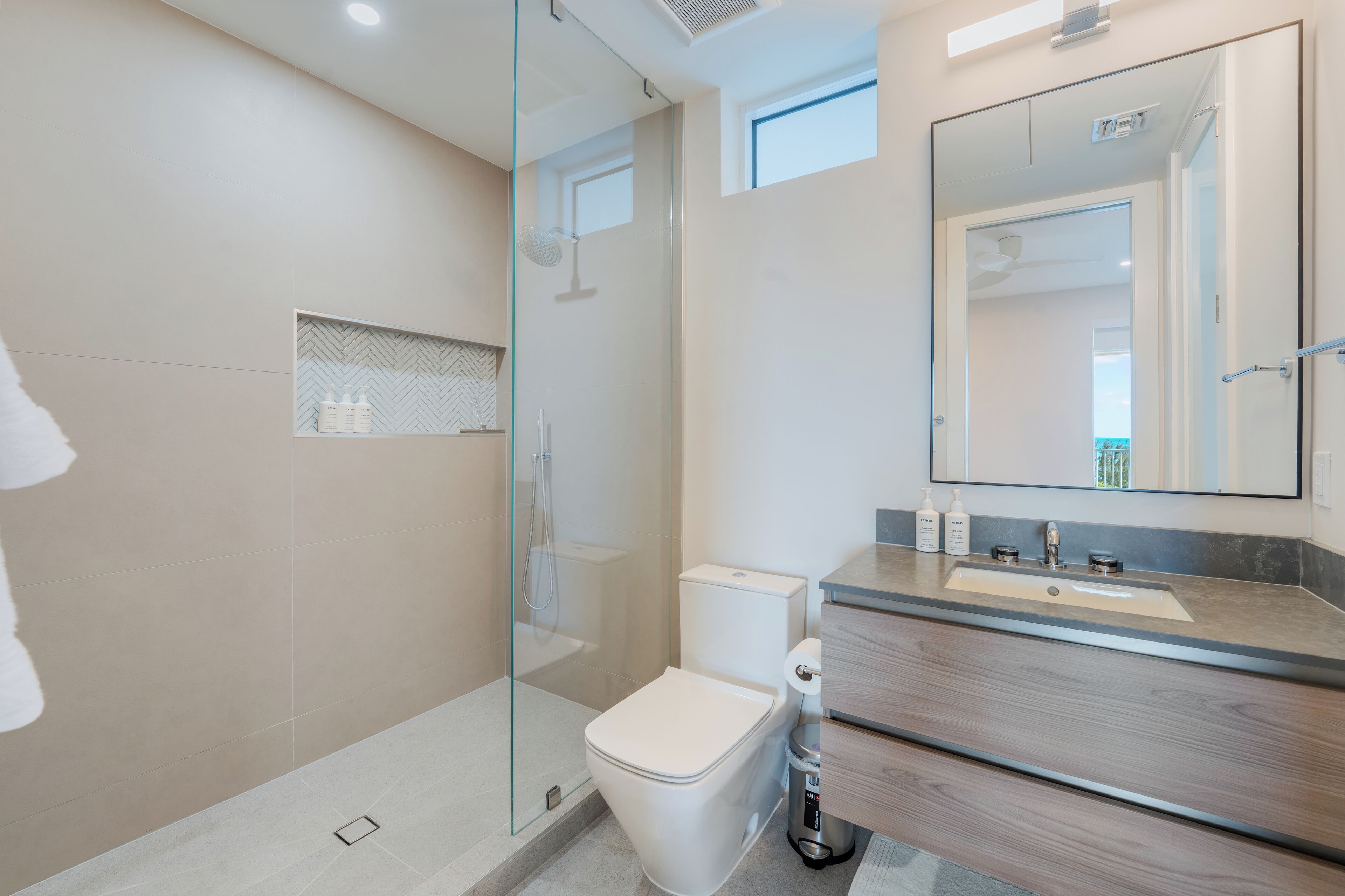 A modern bathroom with a glass-enclosed shower, a white toilet, and a wooden vanity with a mirror.