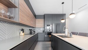 A modern kitchen with a central island, built-in appliances, and pendant lighting. - Point West Premier Rentals (West Bay)