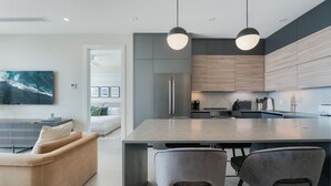 A modern kitchen with a central island, pendant lighting, and a dining area with a sofa and chairs. - Point West Premier Rentals (West Bay)