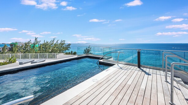 A pool with a wooden deck and a glass railing overlooking the ocean. - Point West Premier Rentals (West Bay)