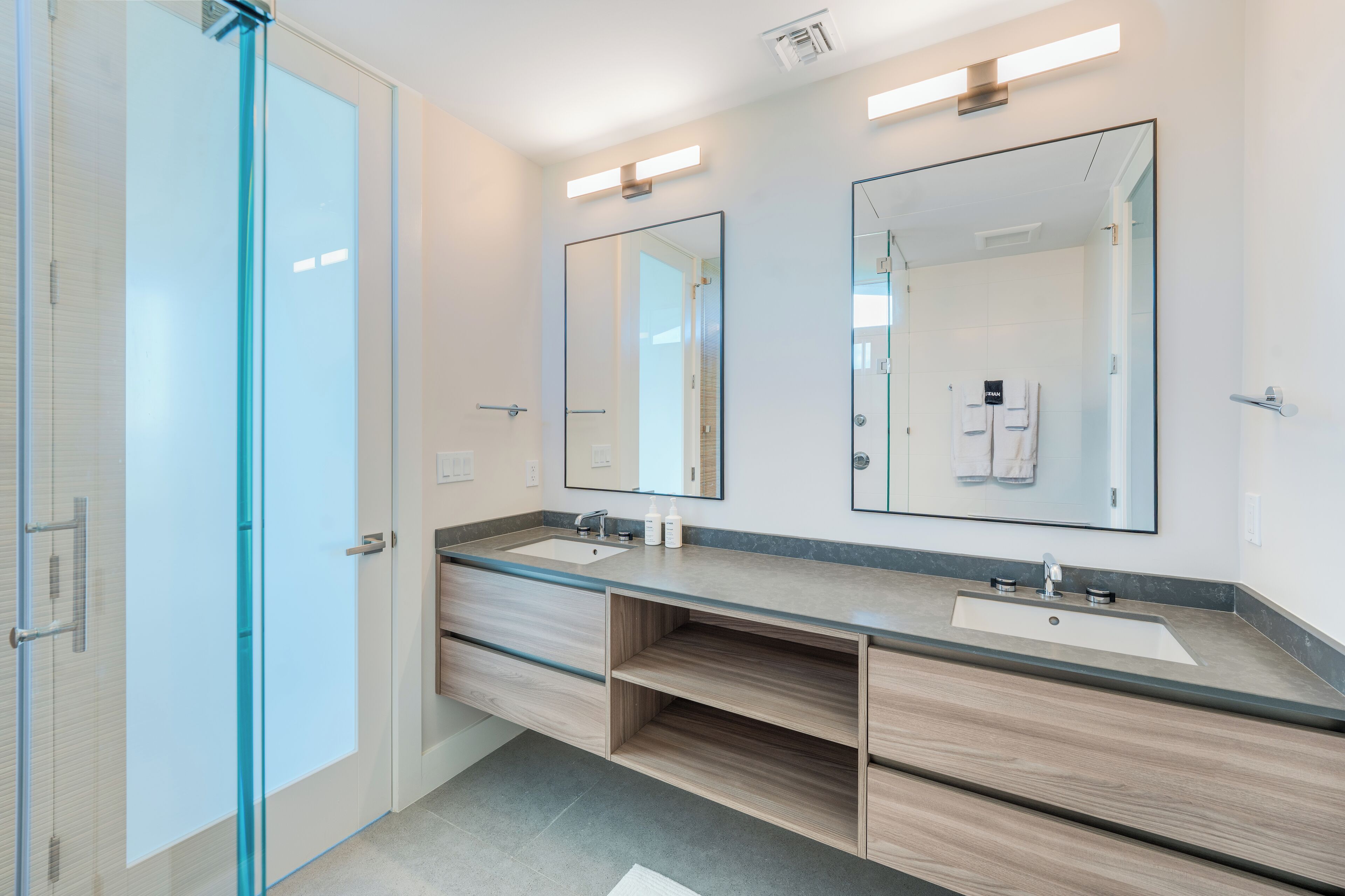 Une salle de bain moderne avec deux vasques, une douche à l’italienne en verre et un grand miroir.