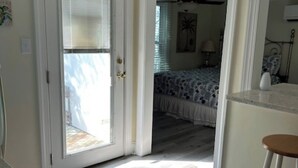 A room with a wooden floor, a bed with a patterned bedspread, a desk with a stool, and a door leading to another room. - Beaufort Bunkhouse (Beaufort)