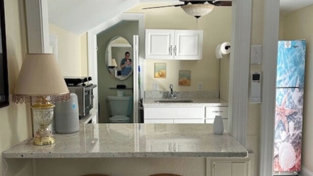 A kitchen with a central island, two bar stools, white cabinets, a refrigerator with a decorative cover, and a visible hallway leading to another room. - Beaufort Bunkhouse (Beaufort)