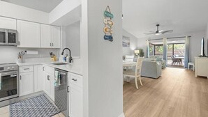 Une cuisine moderne avec des meubles blancs, un four à micro-ondes et un évier. On y trouve également un coin repas avec une table et des chaises, ainsi qu'un ventilateur de plafond.